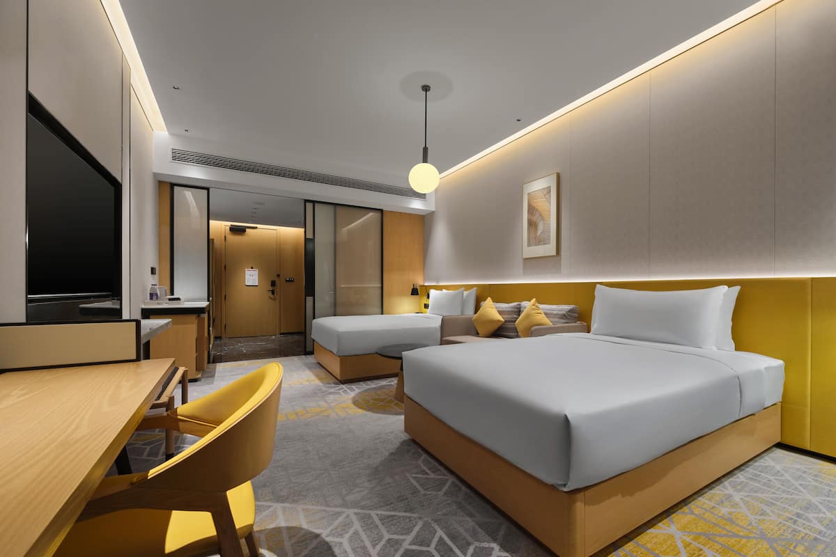 Ein modernes Hotelzimmer mit einem Bett, einem Schreibtisch und einem Stuhl. Eine Tür führt zu einem Badezimmer und einem Flur.