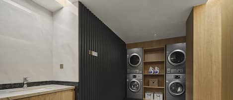 Une buanderie moderne dotée d’un lave-linge et d’un sèche-linge encastrés, d’un évier surmonté d’un plan en marbre et de meubles en bois.