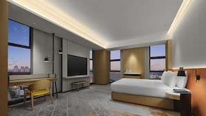 Une chambre d’hôtel moderne dotée d’un grand lit, d’un bureau avec un téléviseur à écran plat, d’un banc et offrant une vue sur le paysage urbain.