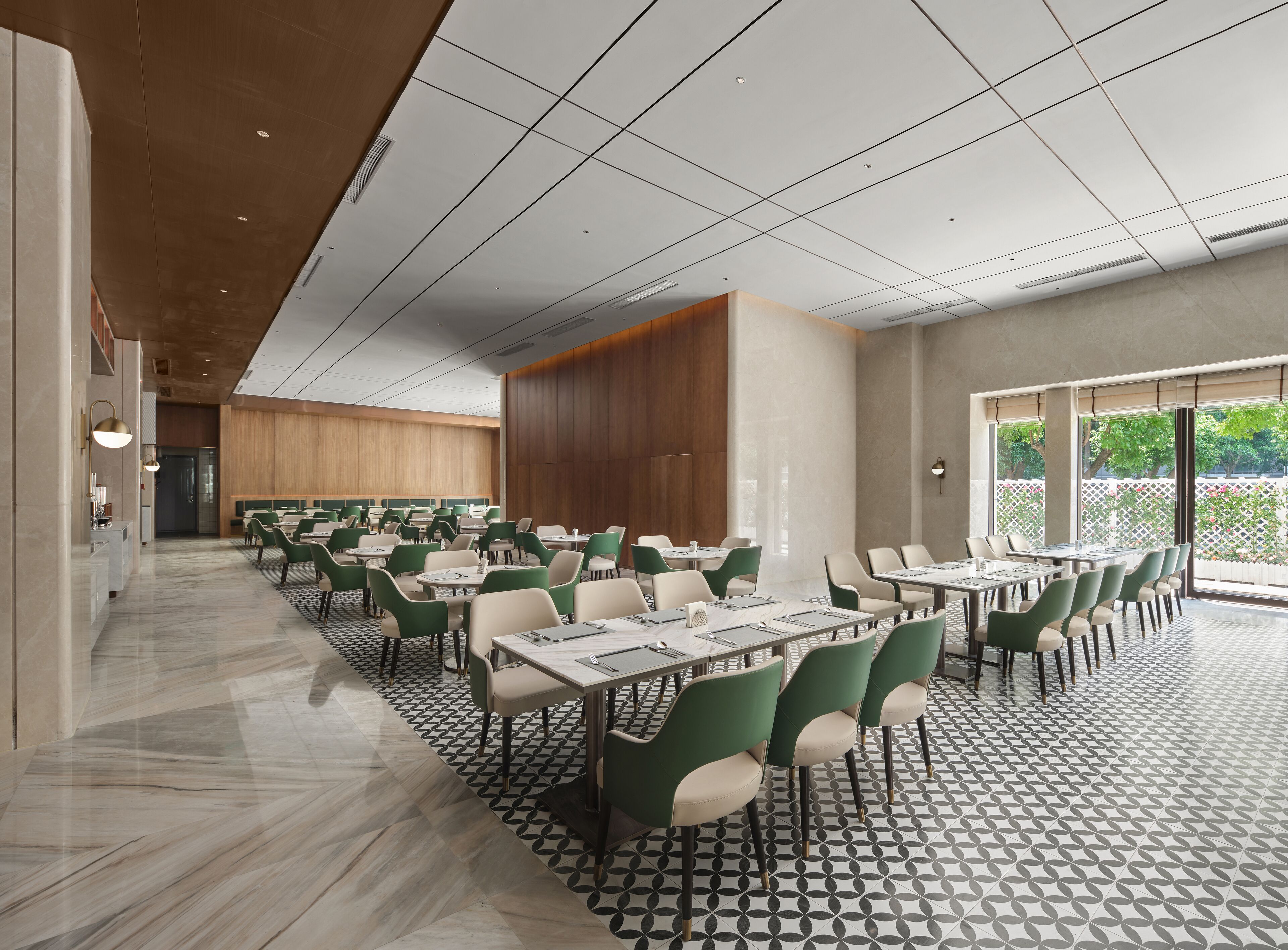 A spacious dining area with multiple tables and chairs, a patterned floor, and large windows providing natural light.