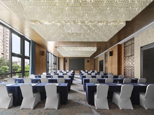 A conference room with rows of tables, large windows, and a decorative ceiling.