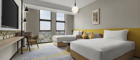 Une chambre d’hôtel moderne, dotée d’un grand lit, d’un bureau et d’une chaise. De grandes fenêtres offrent une vue sur la ville.