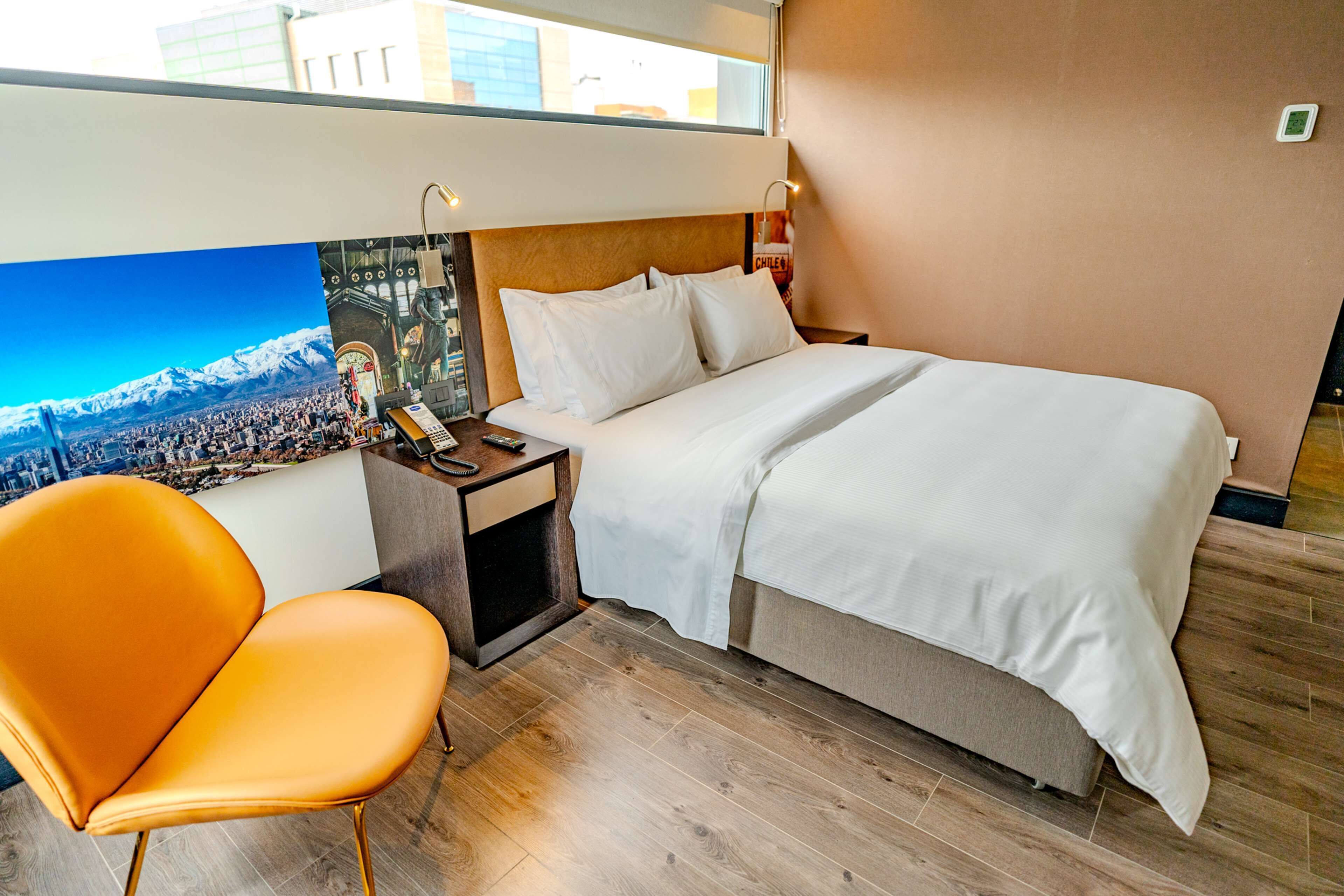 A hotel room with a bed, a nightstand, a chair, and a large poster of a cityscape.