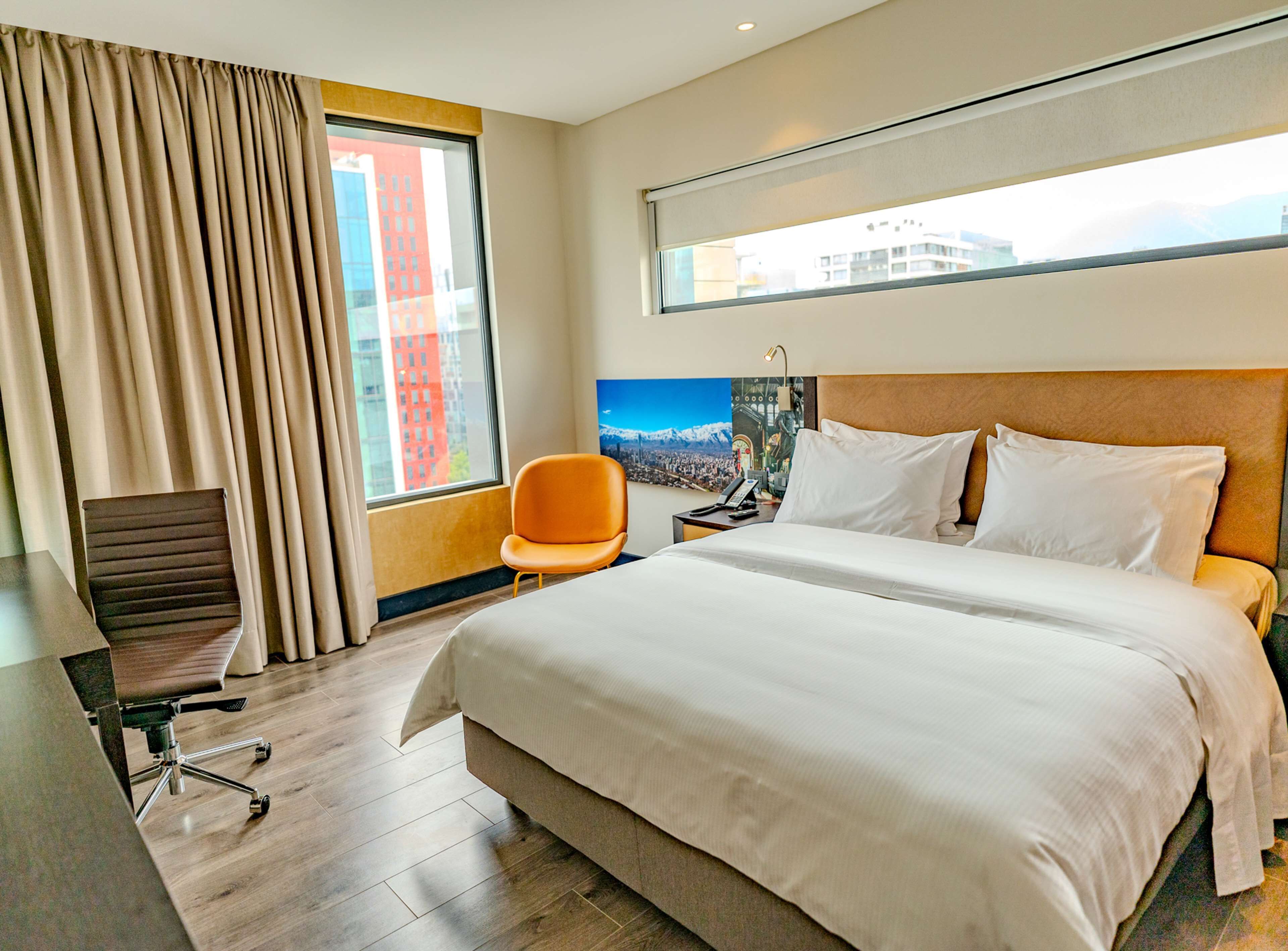 Une chambre d’hôtel avec un grand lit, un bureau avec une chaise, une fenêtre avec des rideaux et un tableau au mur.