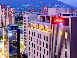 A hotel with a prominent red neon sign, modern architecture, and a view of surrounding buildings and mountains. - Hampton By Hilton Santiago Las Condes (Santiago)