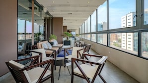 Een moderne lounge met zitplaatsen en een televisie, grote ramen en uitzicht op de stad.