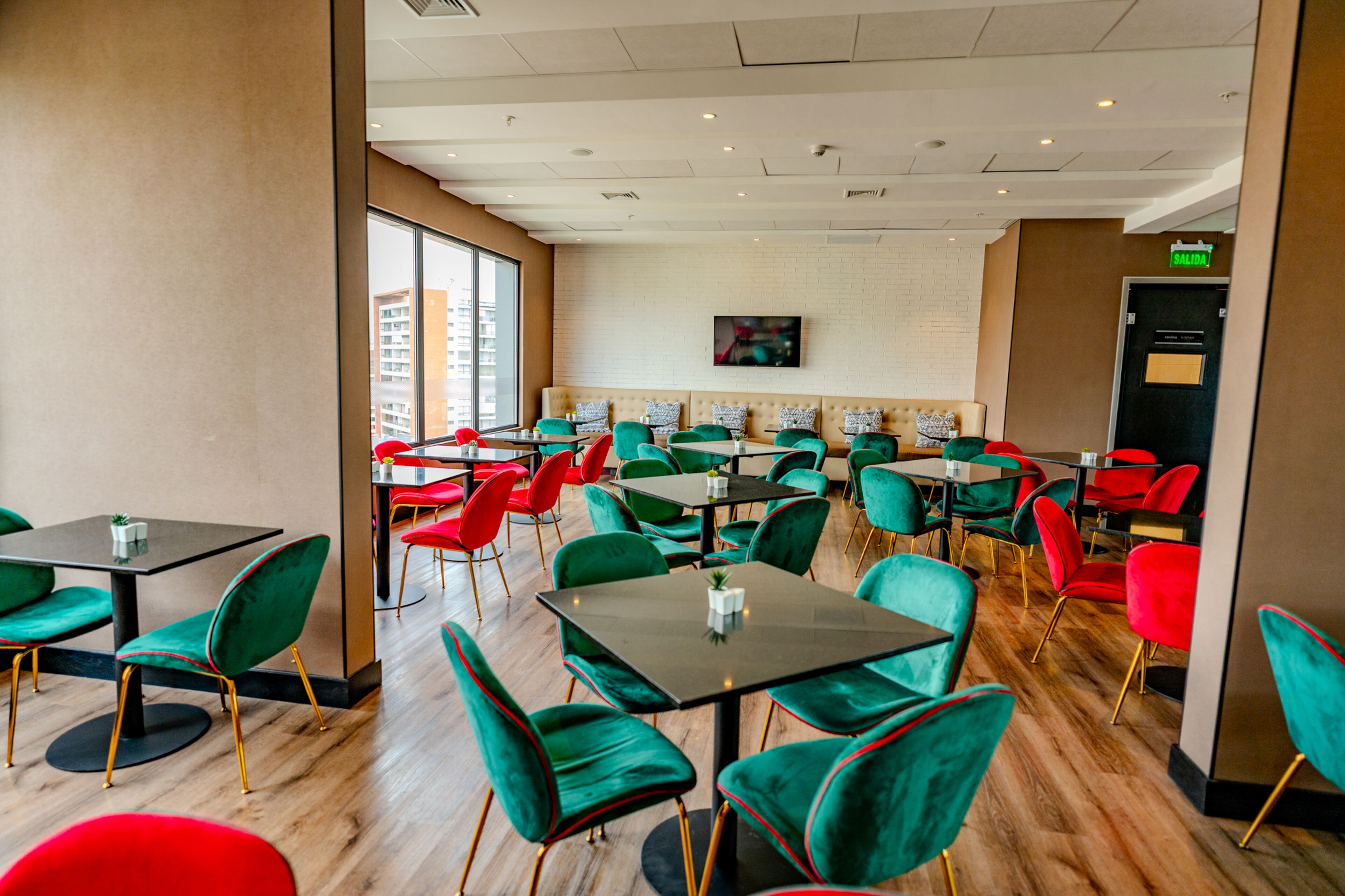 Un restaurante con sillas y mesas verdes y rojas, y una pared de ladrillo con un televisor.