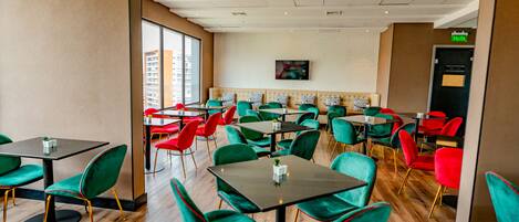 Un restaurante con sillas y mesas verdes y rojas, y una pared de ladrillo con un televisor.