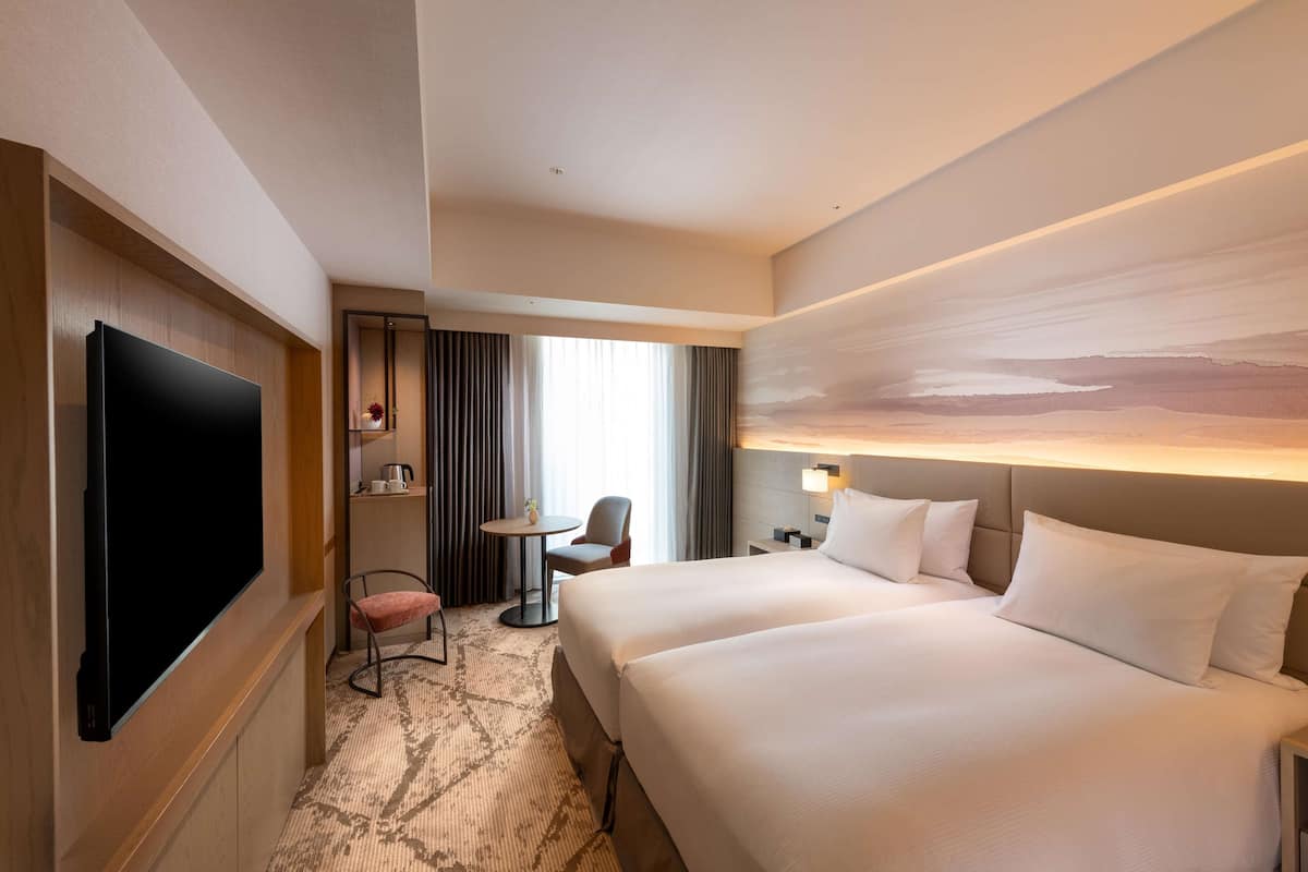 A hotel room with a large bed, a flat-screen TV, a small table, a chair, and a painting on the wall.