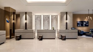 A modern hotel lobby with three reception desks, a large wall-mounted TV, and a seating area with a sofa and coffee table. - DoubleTree by Hilton Toyama (Toyama)