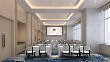 A conference room with rows of white tables and chairs, a projector screen with 'DOUBLETREE' logo, and a blue carpet with white patterns.