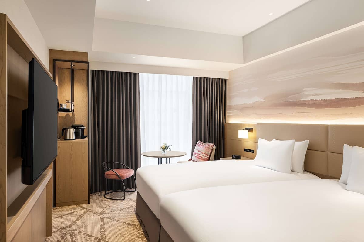 A hotel room with a large bed, a flat-screen TV, a small table with a chair, and a window with curtains.