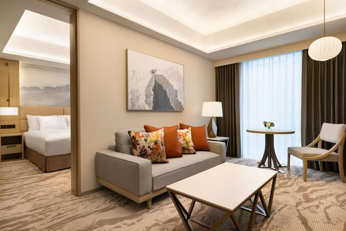 A hotel room with a sofa, a bed, a coffee table, a lamp, and a painting on the wall.