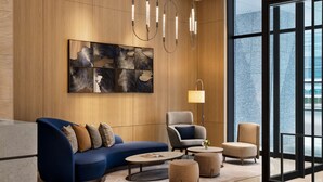 A modern lobby with a curved blue sofa, a grey armchair, and a beige armchair. There is a round coffee table with a magazine, a floor lamp, and a large abstract painting on the wall. - DoubleTree by Hilton Toyama (Toyama)