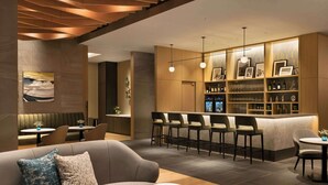 A modern bar area with a counter, bar stools, and a display of bottles and glasses. - DoubleTree by Hilton Toyama (Toyama)