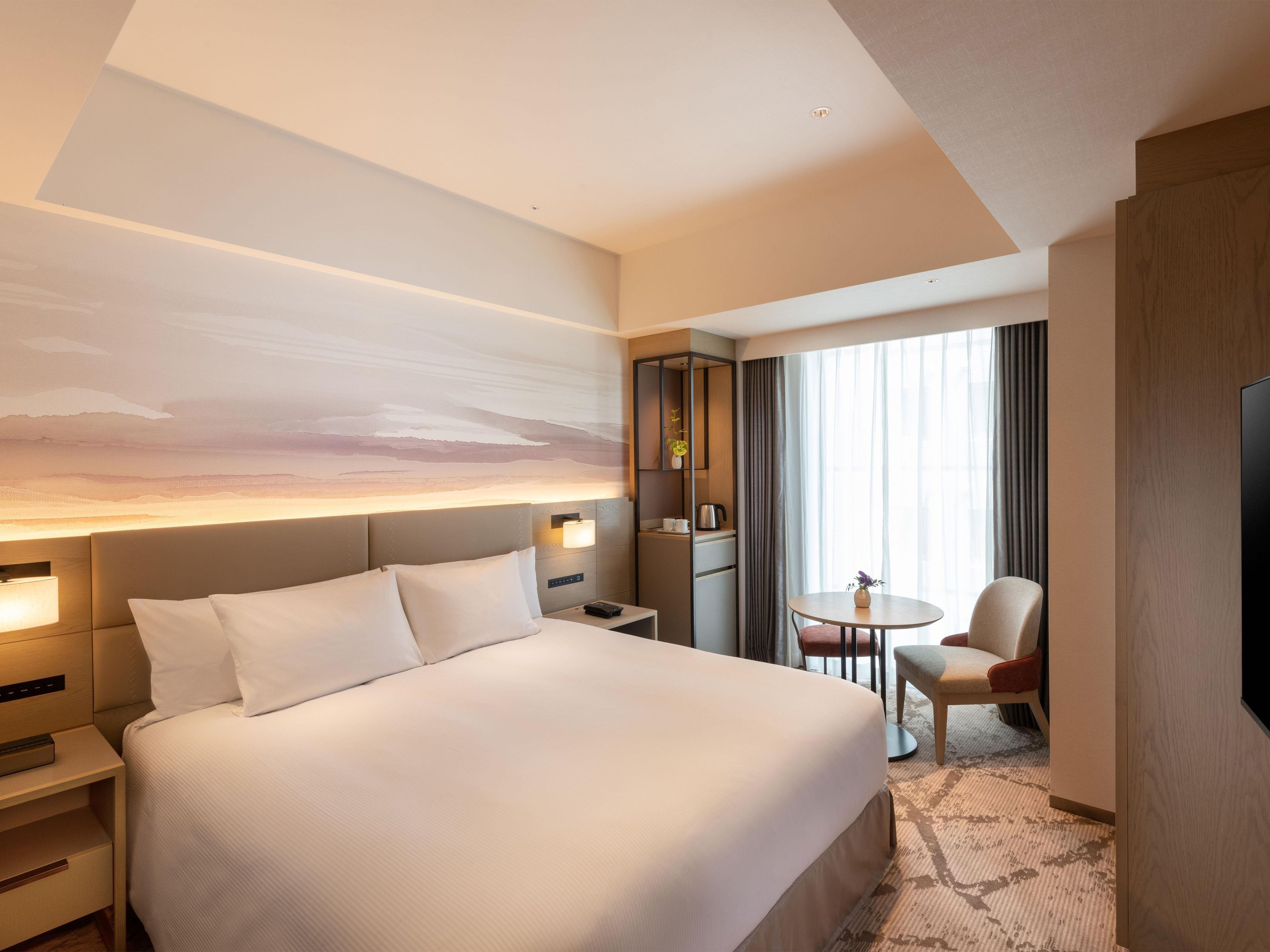Une chambre d’hôtel avec un grand lit, des tables de chevet, un bureau, une chaise, une télévision et une fenêtre avec des rideaux.