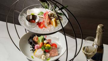 A multi-tiered glass dish with seafood and vegetables, a small bowl of sauce, and a bottle of wine.