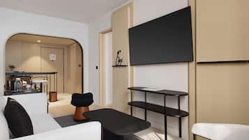 Una sala de estar moderna con un sofá, una mesa de centro, un televisor montado en la pared y una pequeña zona de cocina al fondo.