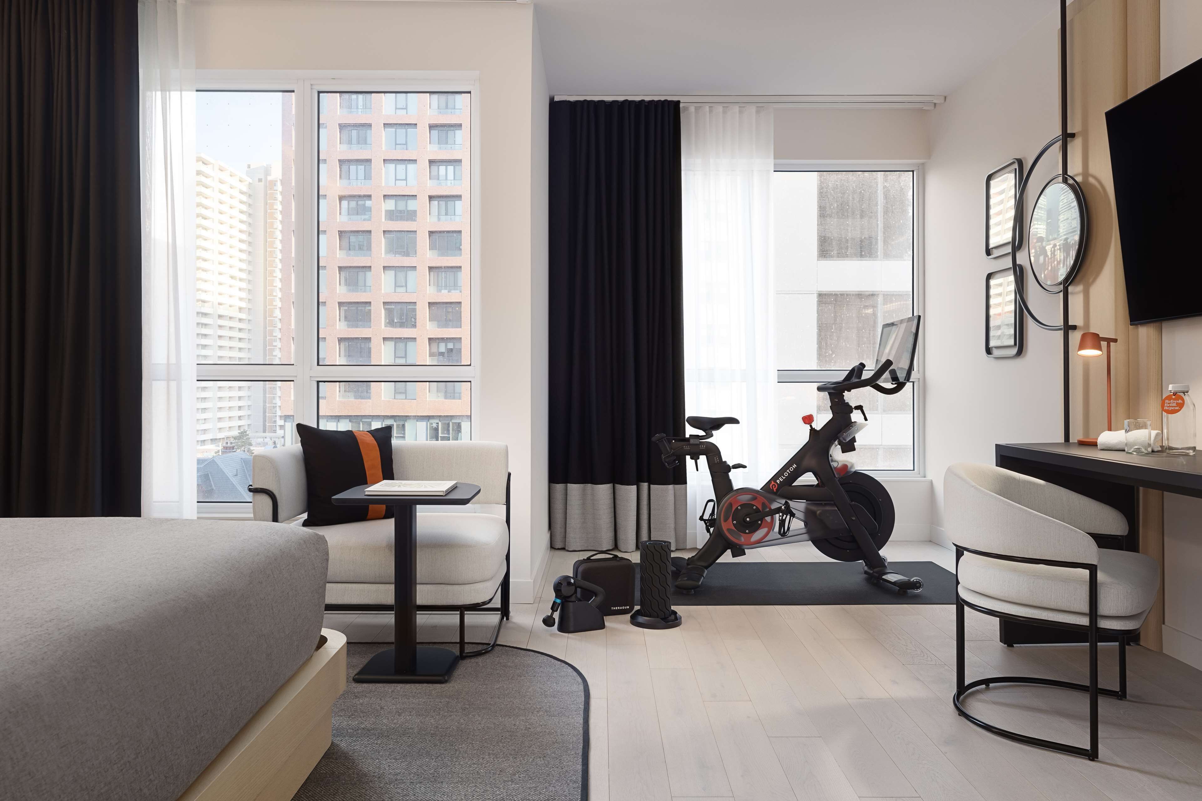 A hotel room with a bed, a desk, a chair, an exercise bike, and a TV.