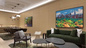 A modern hotel lobby with a dining area, a green sofa, and a large cityscape painting.