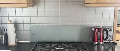 Une cuisine équipée d’une cuisinière à gaz, de meubles en bois, d’une bouilloire en acier inoxydable et d’une hotte en verre.