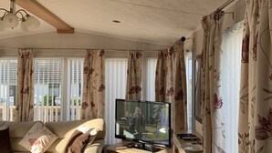 A living room with a sofa, TV, and wooden ceiling beams. - Immaculate 2-bed Lodge in Monreith (Newton Stewart)