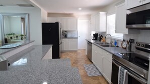 Una cocina moderna con armarios blancos, un refrigerador negro, electrodomésticos de acero inoxidable y una encimera de granito.
