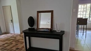Una consola negra amb un mirall i objectes decoratius, un sòl de rajoles i una porta al fons.