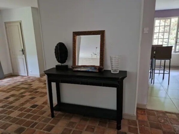 Una consola negra con espejo y objetos decorativos, suelo de baldosas y una puerta al fondo.