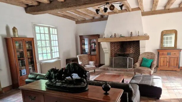Un saló rústic amb bigues de fusta a la vista, una llar de foc, sofàs de pell i un armari de fusta.