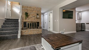 Een moderne woonkamer met een stenen openhaard, een houten salontafel en een trap.