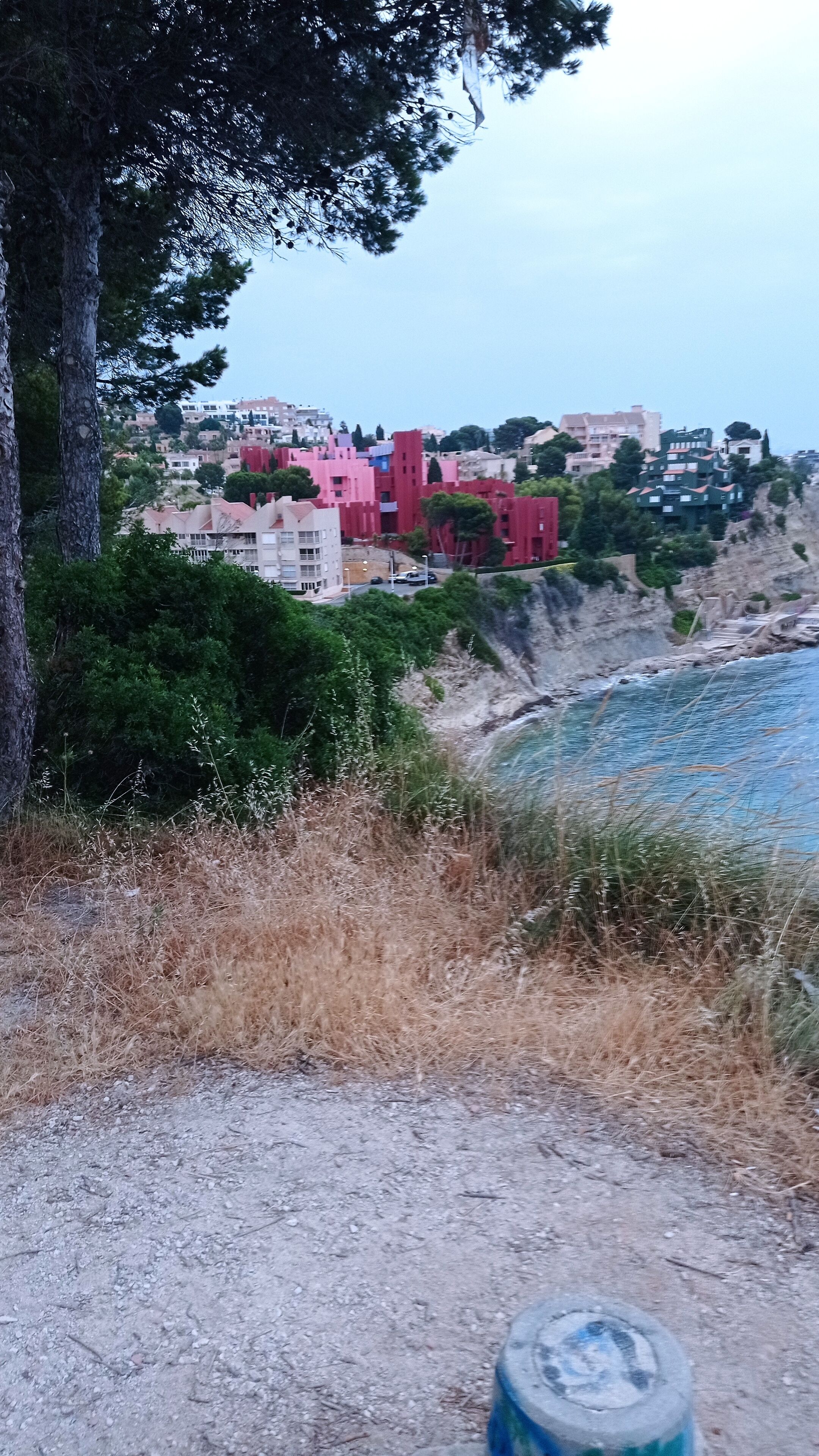 A coastal town with buildings on a hillside, a beach in the foreground, and a clear sky.