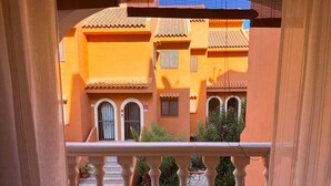 Ein Balkon mit Steinbalustrade mit Blick auf einen Innenhof mit Fliesenböden und Topfpflanzen.