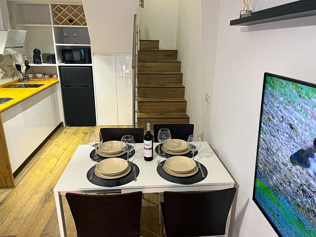 A dining area with a table set for four, a refrigerator, a microwave, and a TV on the wall.
