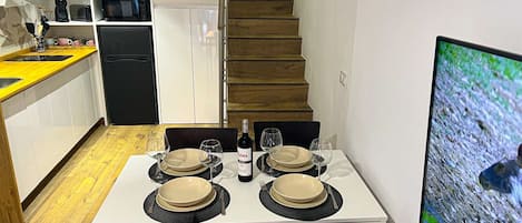 A dining area with a table set for four, a refrigerator, a microwave, and a TV on the wall.