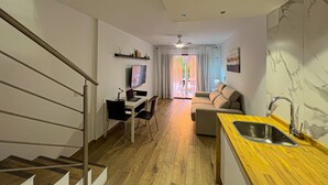 Eine moderne Wohnung mit Treppe, einem Wohnzimmer mit Sofa und Fernseher, einer Küche mit Spüle und einem Essbereich.