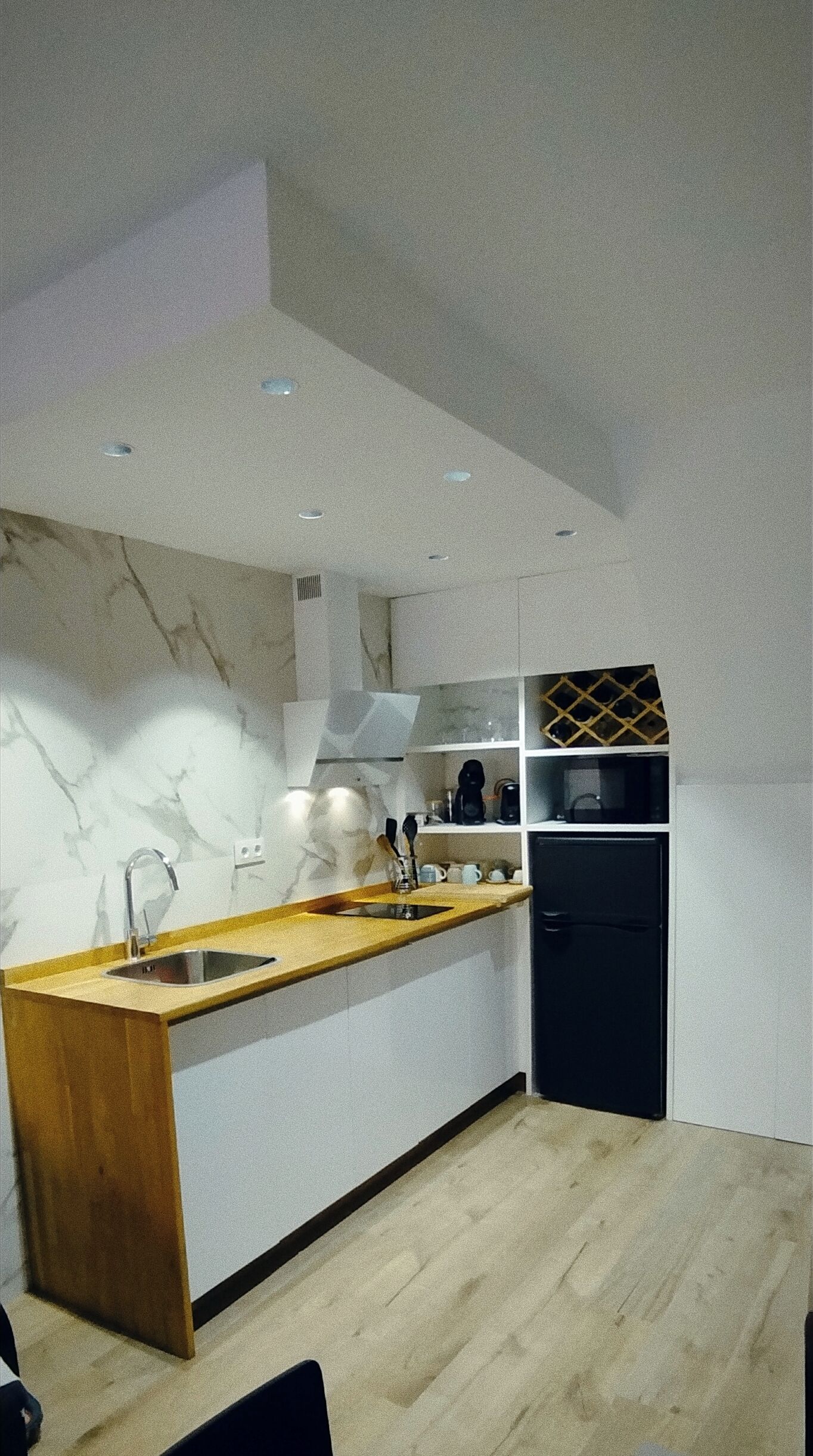 A modern kitchen with a marble backsplash, wooden countertop, and a black refrigerator.