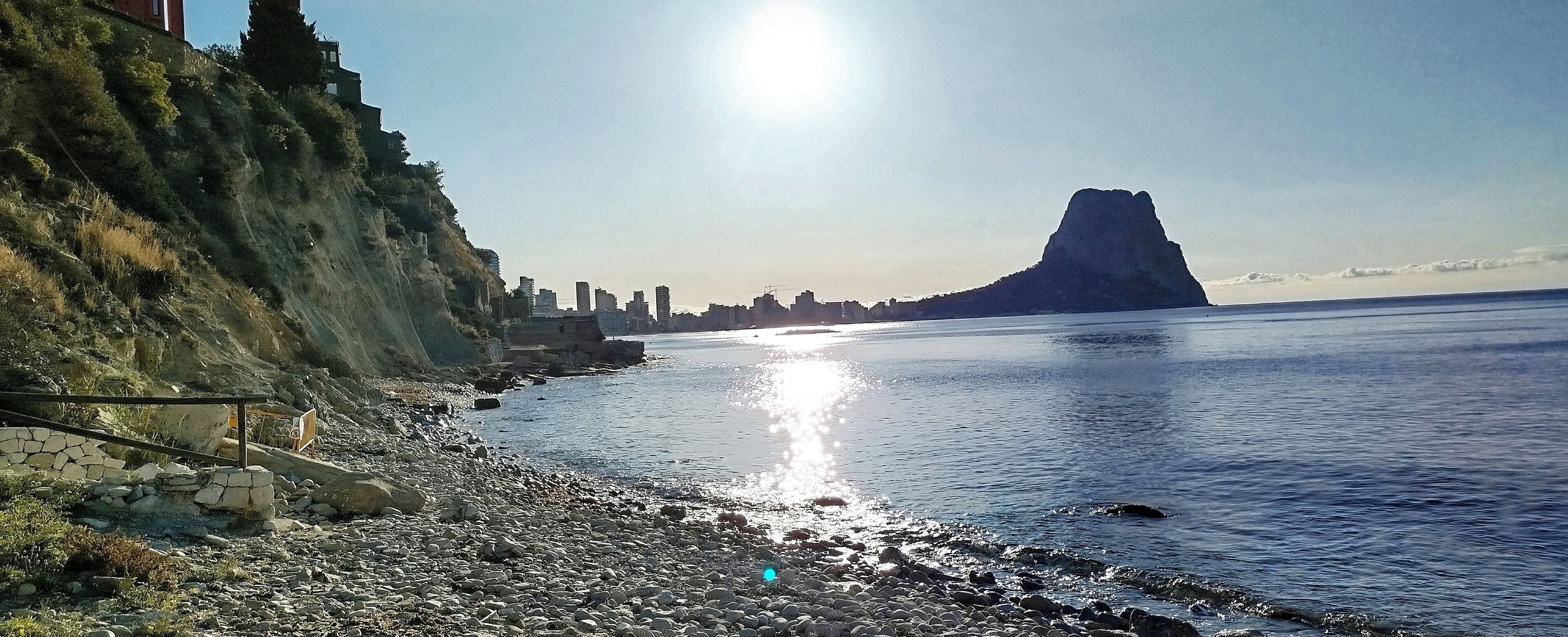 Une plage de galets avec, en arrière-plan, le profil d’une ville et un sommet montagneux imposant.
