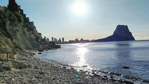 Ein felsiger Strand mit Stadtansicht im Hintergrund und einem markanten Berggipfel.