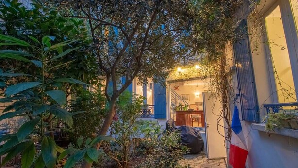 A courtyard with a staircase leading to an upper level, surrounded by lush greenery and a flag. - Private House and Garden in Paris (Paris)