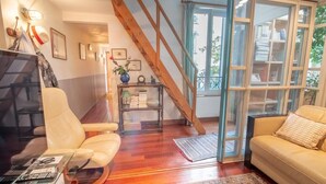 A cozy living room with a wooden staircase, a sofa, a chair, a coffee table, and a bookshelf. - Private House and Garden in Paris (Paris)
