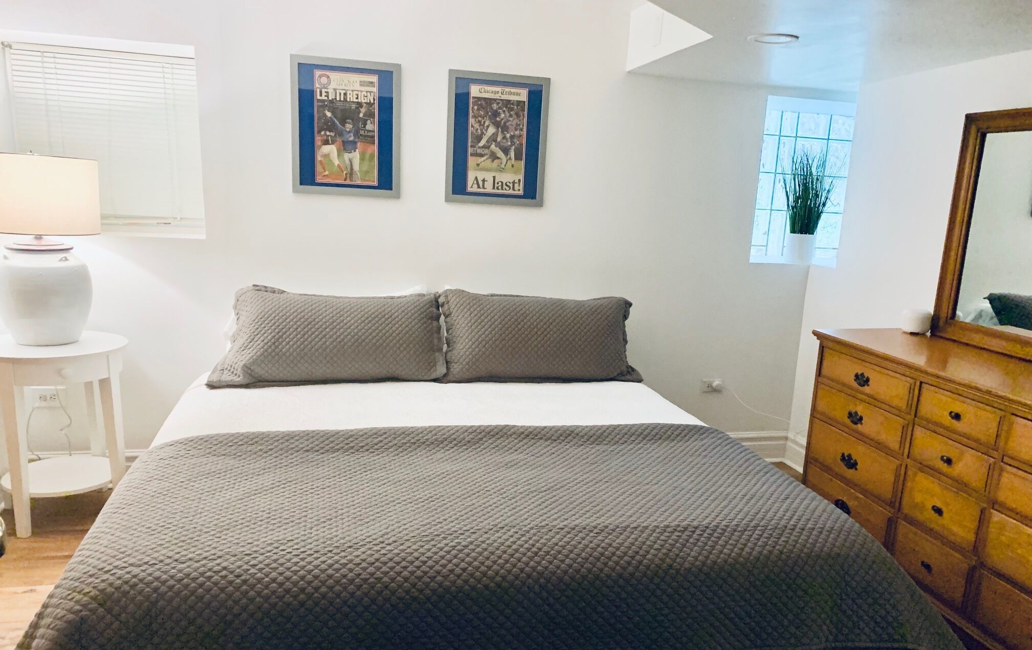 A bedroom with a bed, two posters on the wall, a dresser, and a lamp.