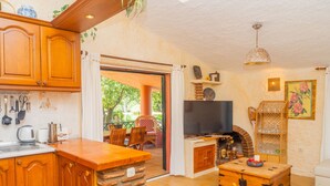 A kitchen with wooden cabinets, a stone column, a television, and a dining area with a table and chairs. - Cubo's Finca La Fuente del Pedregal Casa 3 / nature / community pool / free Wi-Fi (Coín)