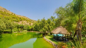 A tranquil pond with a gazebo, surrounded by lush greenery and a hill in the background. - Cubo's Finca La Fuente del Pedregal Casa 3 / nature / community pool / free Wi-Fi (Coín)