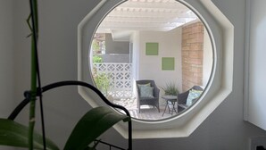 A room with a large octagonal window, a potted plant, and a view of an outdoor patio area with a table and chairs.