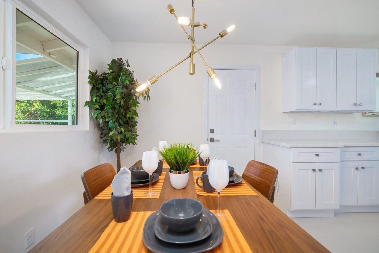 A dining area with a wooden table set for four, a potted plant, and a modern chandelier.