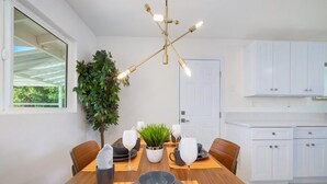 A dining area with a wooden table set for four, a potted plant, and a modern chandelier.