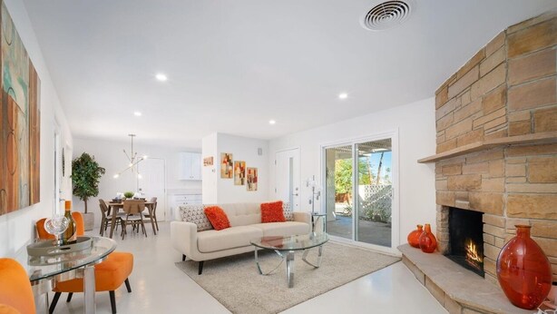 A modern living room with a fireplace, a dining area, and a sofa with orange cushions.