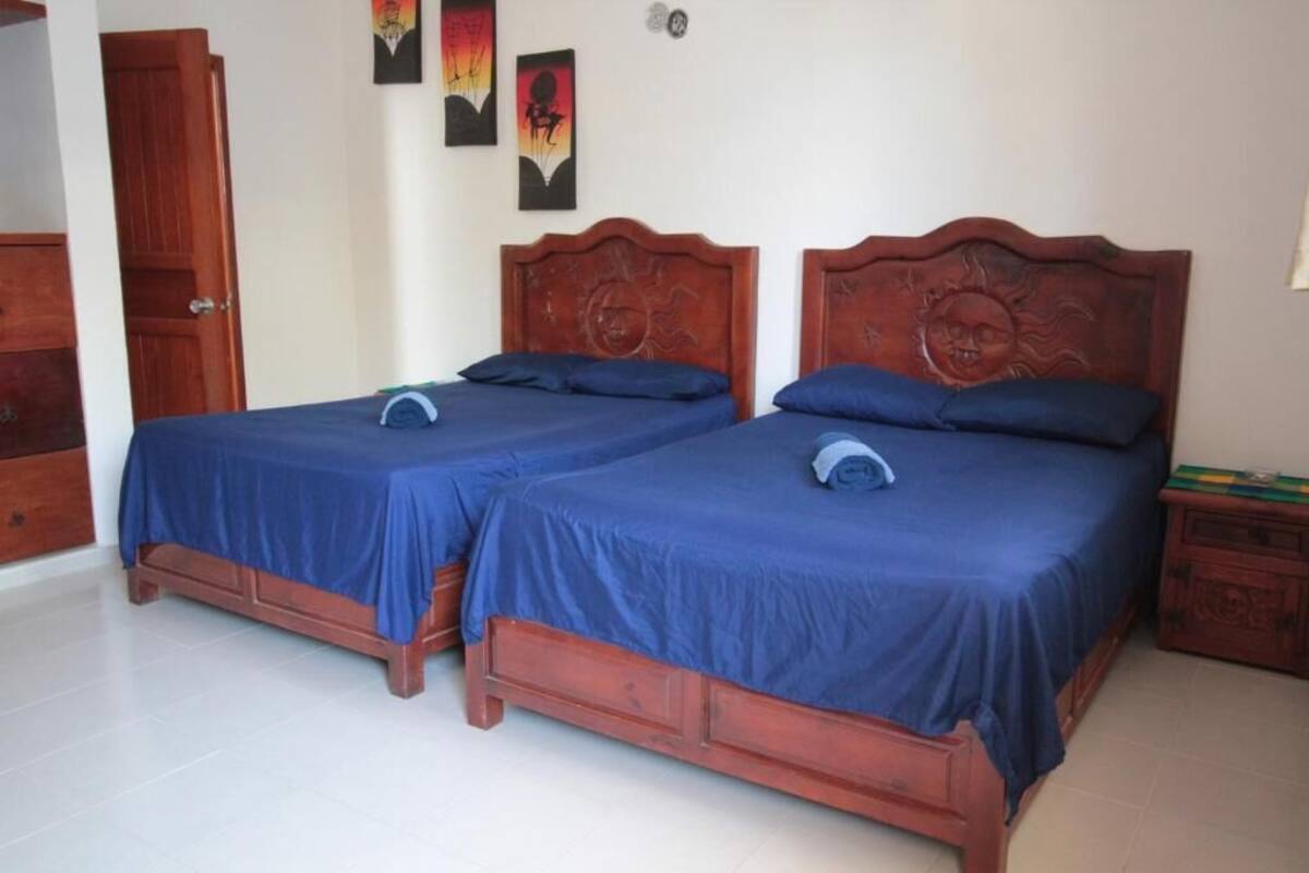 Quarto com duas camas de madeira, roupa de cama azul, um guarda-roupa de madeira e uma pequena mesa com um livro.