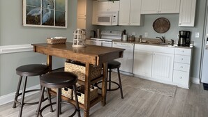 Una cocina con armarios blancos, una mesa de madera con taburetes, un microondas y una cafetera.